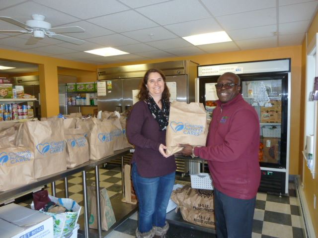 A man and a woman standing in a food pantry holding a Cleaning Authority Cares bag