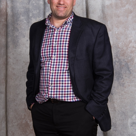 A man smiling with a red and blue checker shirt on smiling in front of the camera